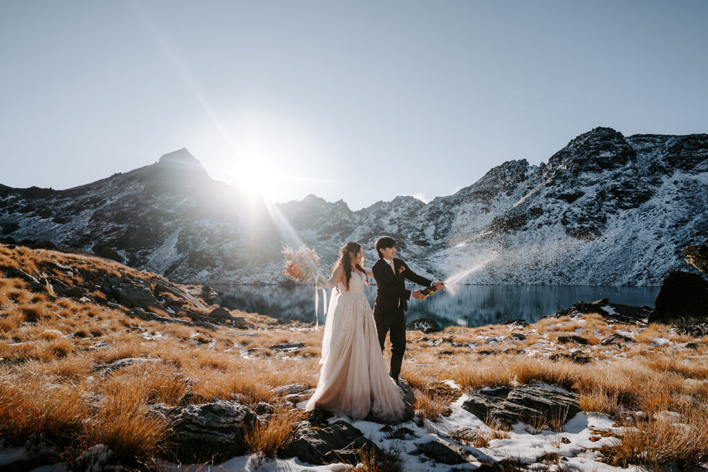 bride and groom popping champagne by lake Hope in queenstown new zealand